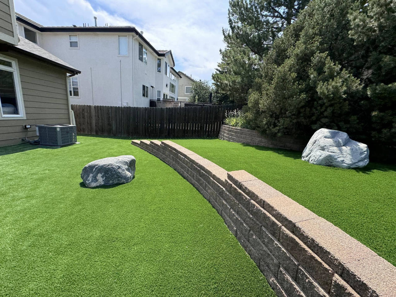 Artificial turf backyard with retaining wall and decorative boulders — artificial turf in Denver, CO